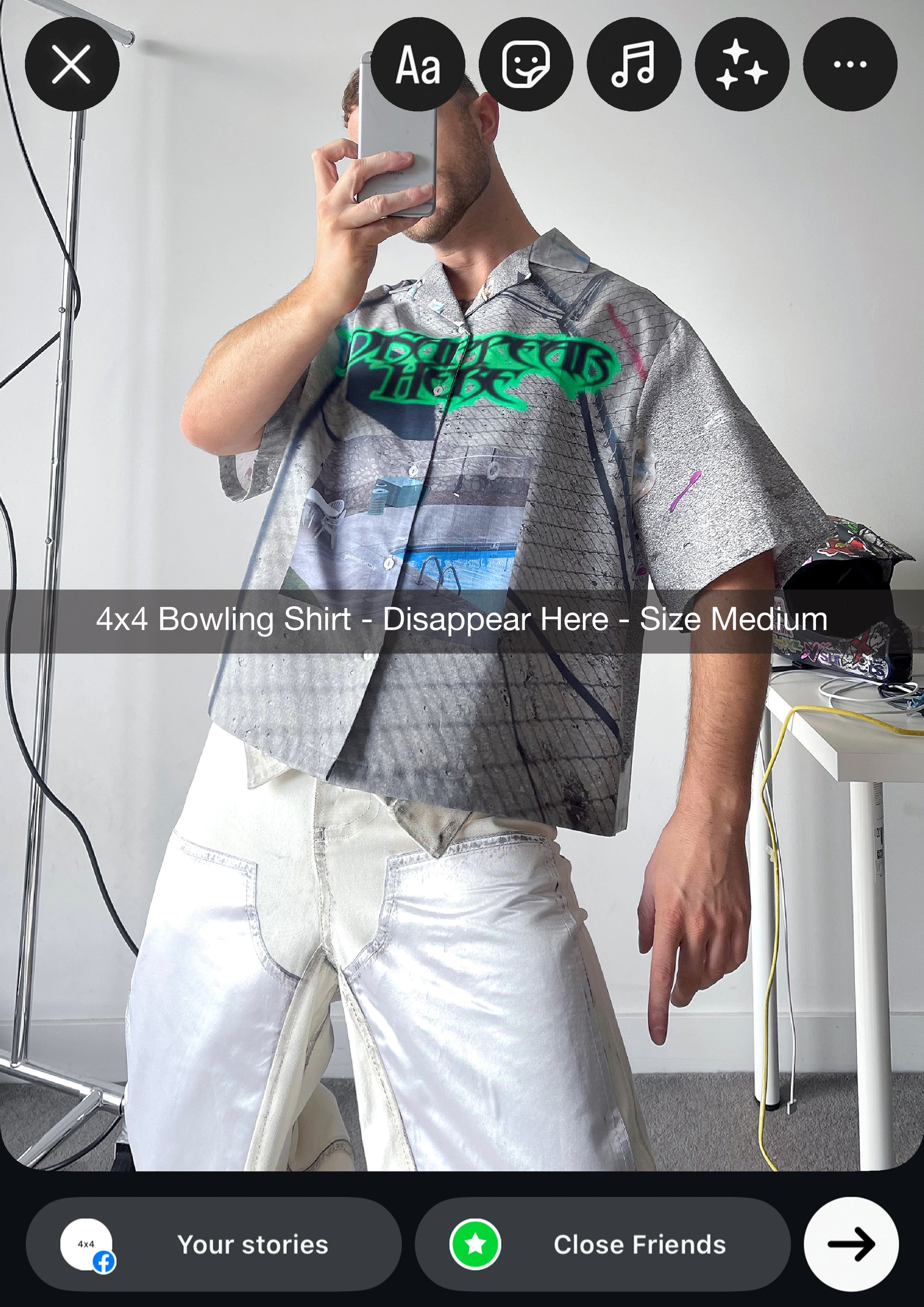 Person wearing a patterned shirt and white pants taking a mirror selfie.