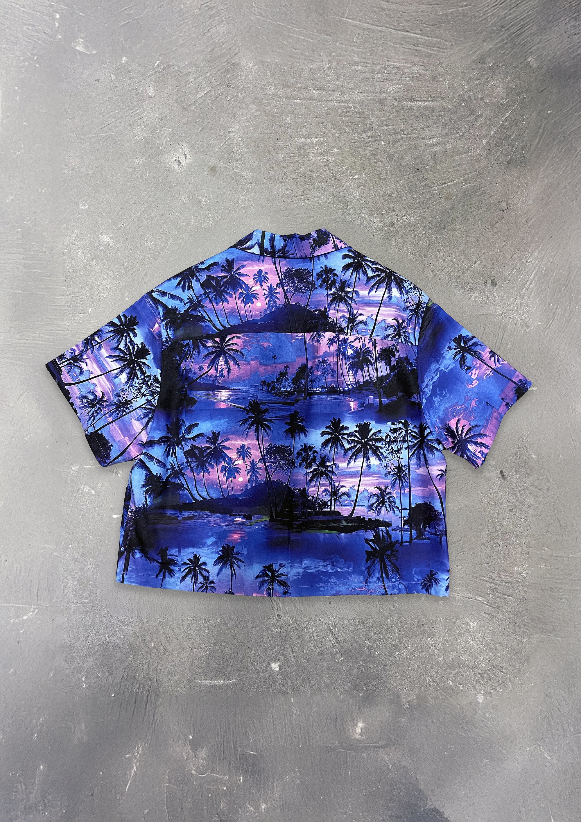 Short-sleeve shirt with palm tree and sunset design on a textured gray background