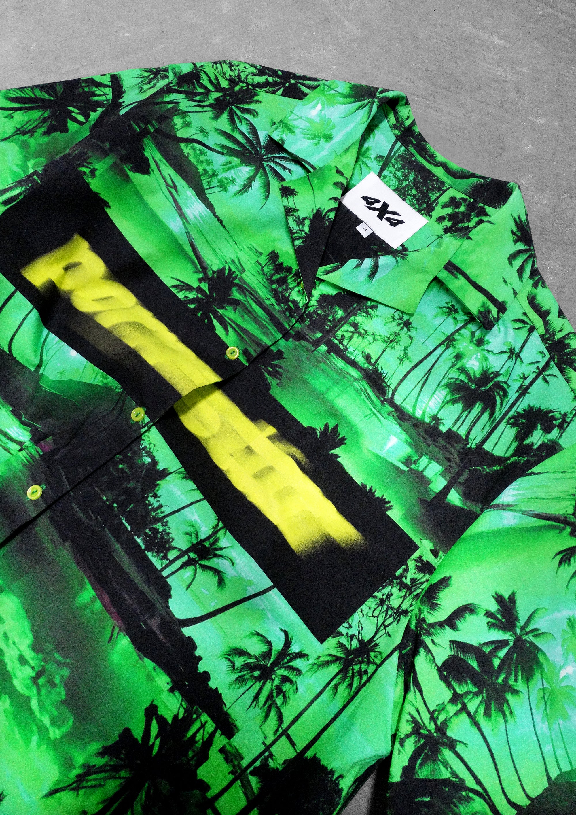 Green shirt with black palm tree pattern and yellow accents on a gray surface