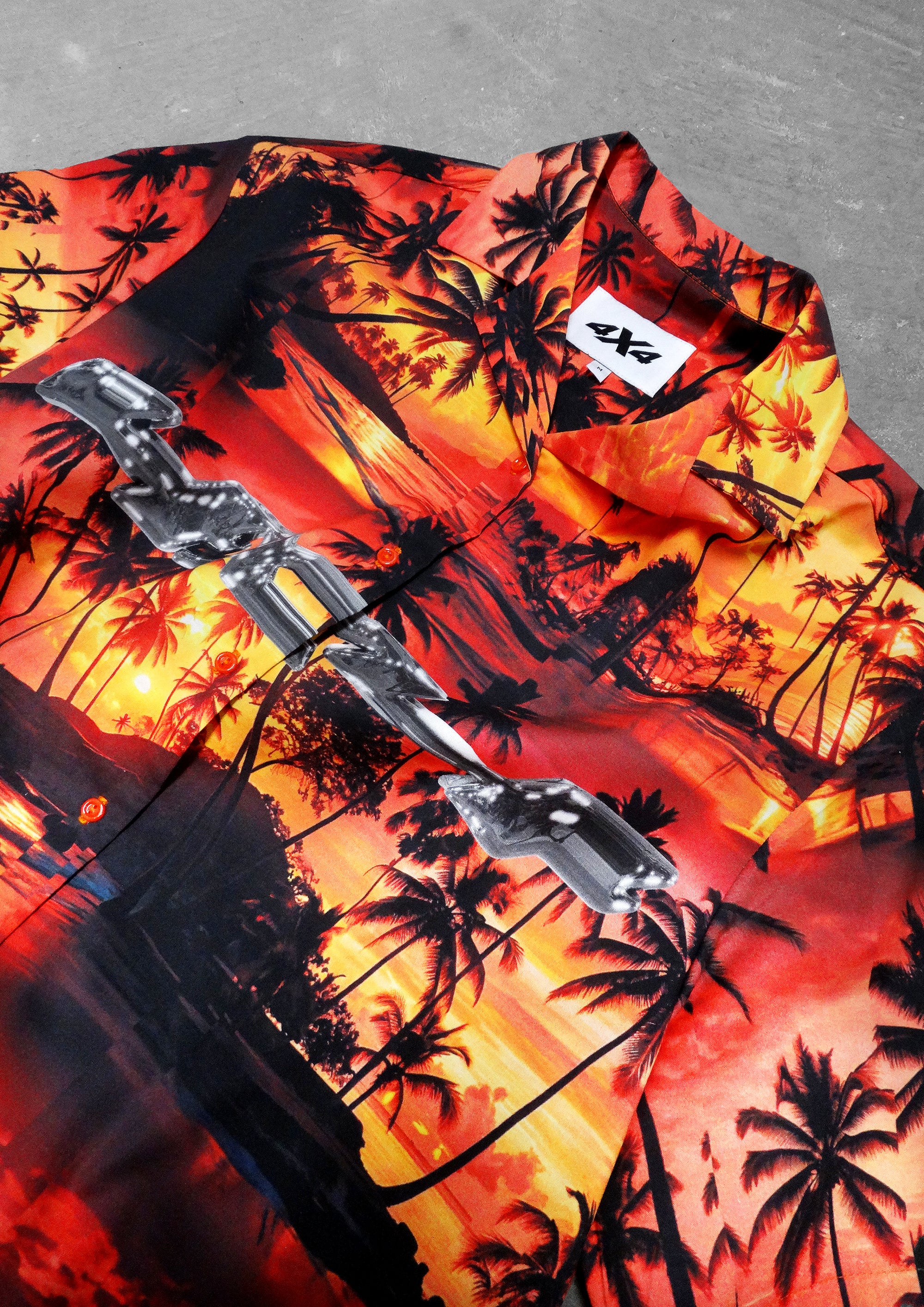 Hawaiian shirt with palm tree design and brand logo on a gray surface
