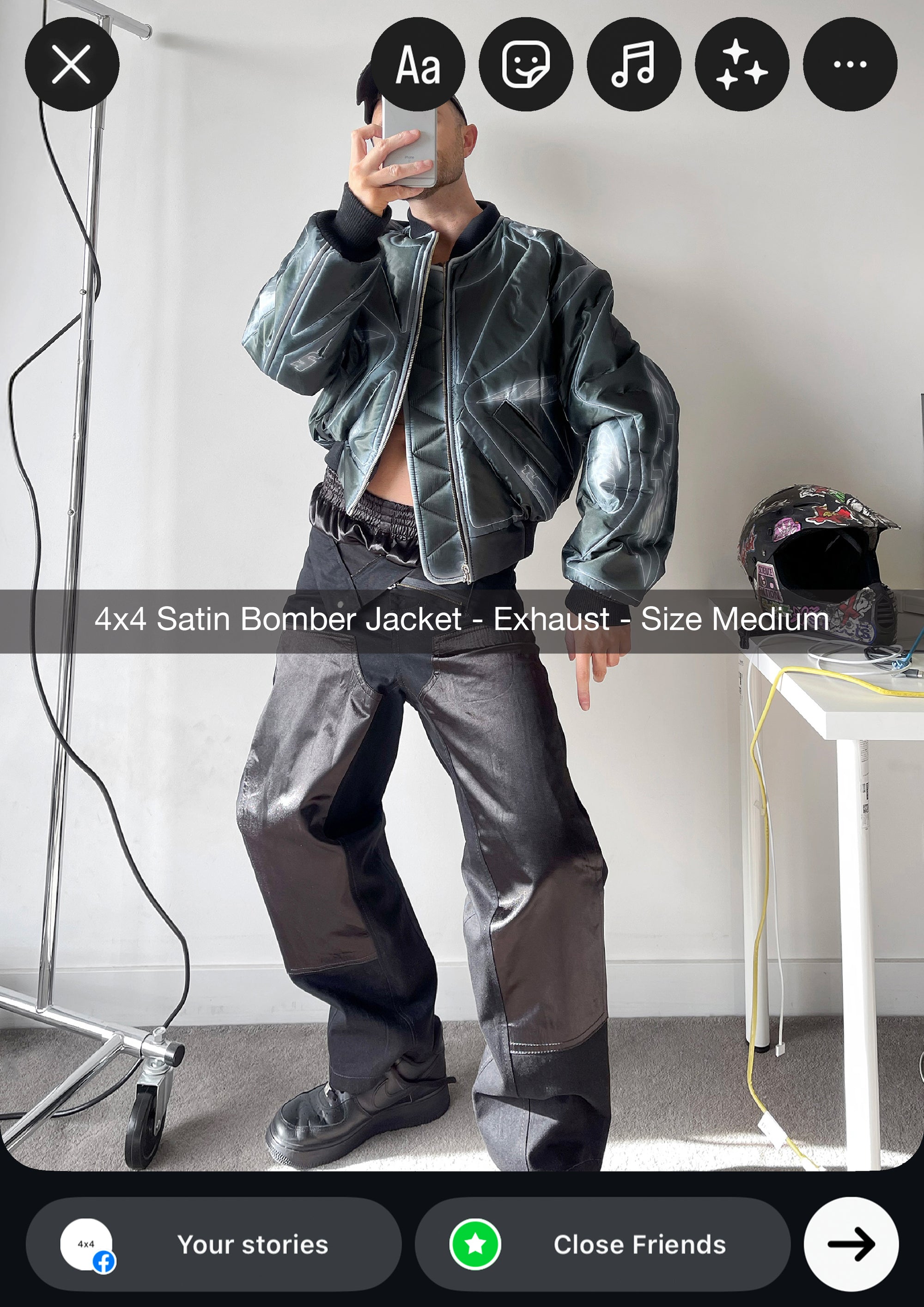 Person wearing a satin bomber jacket in a room with a white wall and a table with a hat.