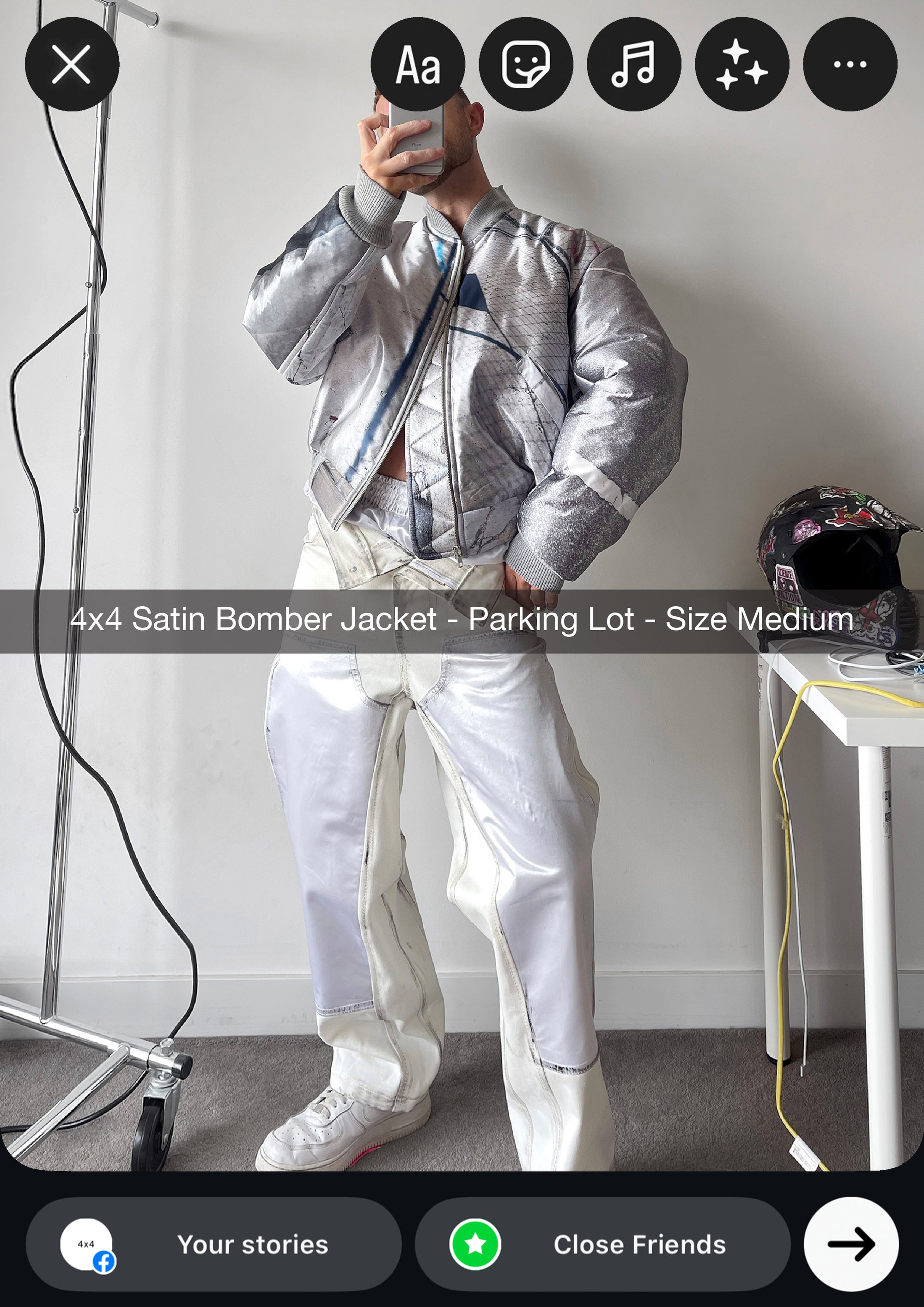 Person wearing a silver satin bomber jacket and white pants in a minimal indoor setting.