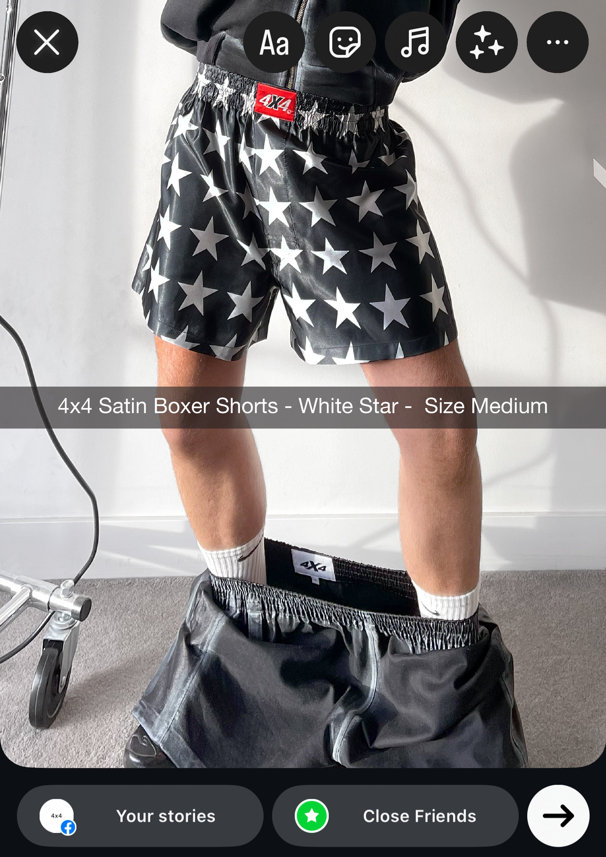 Person wearing black satin boxer shorts with white star pattern on a plain background