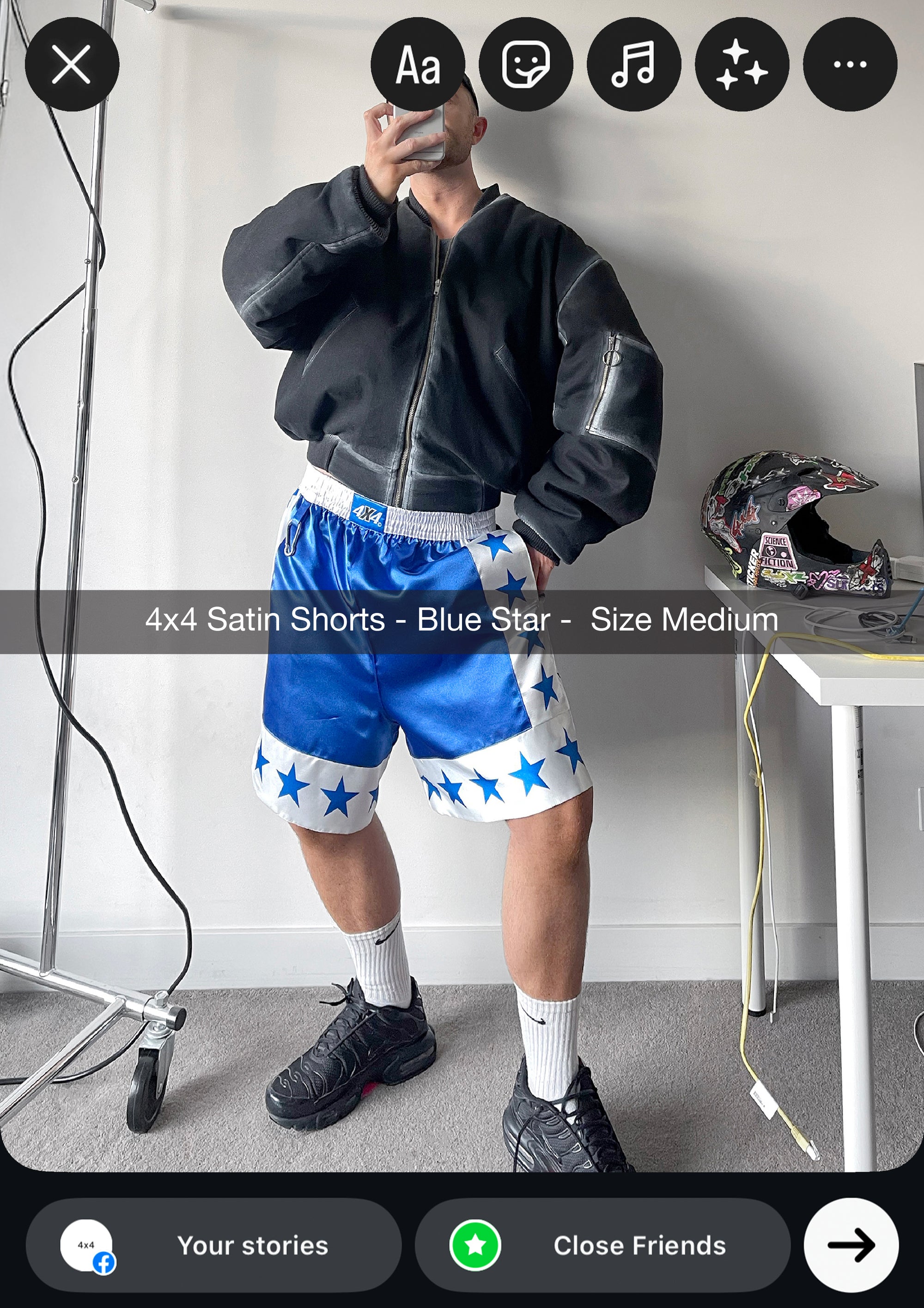 Person wearing blue shorts with star patterns and a black jacket, taking a mirror selfie.