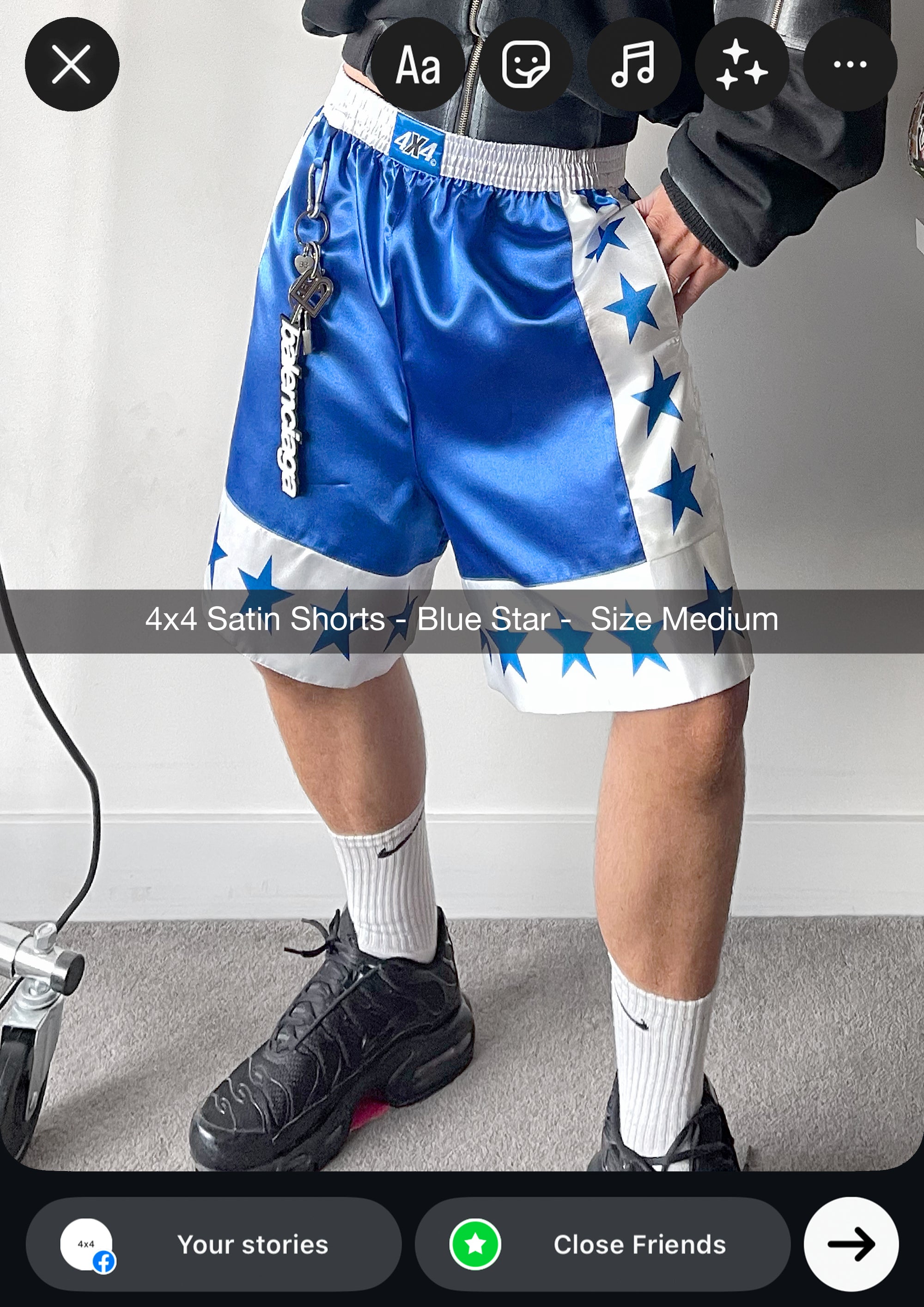 Person wearing blue satin shorts with star patterns and black sneakers on a plain background