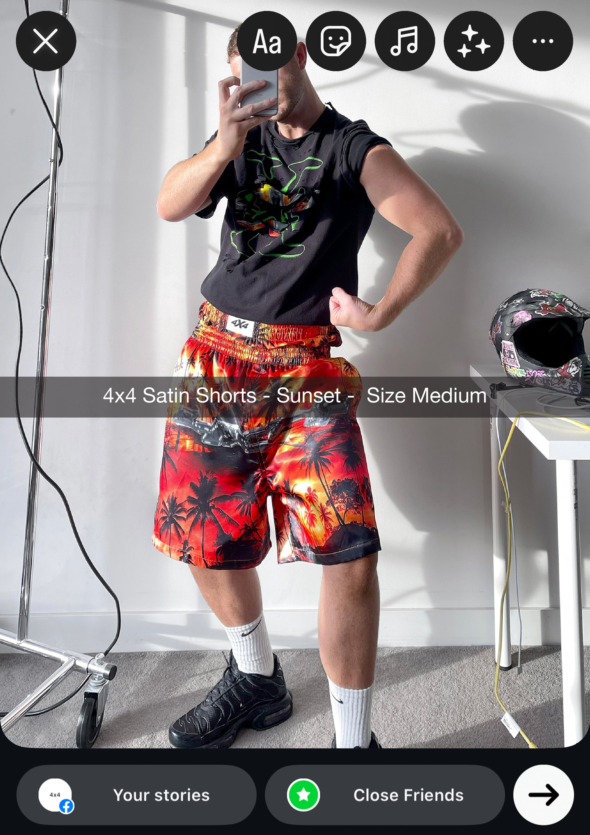 Person wearing a black t-shirt with colorful graphics and red satin shorts with palm tree design, taking a mirror selfie.
