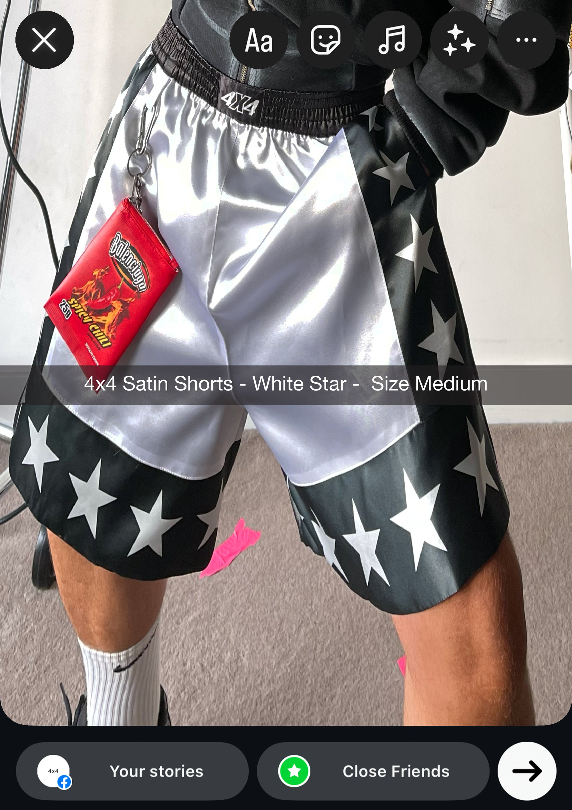 Silver satin shorts with black star pattern worn by a person, on a neutral background.