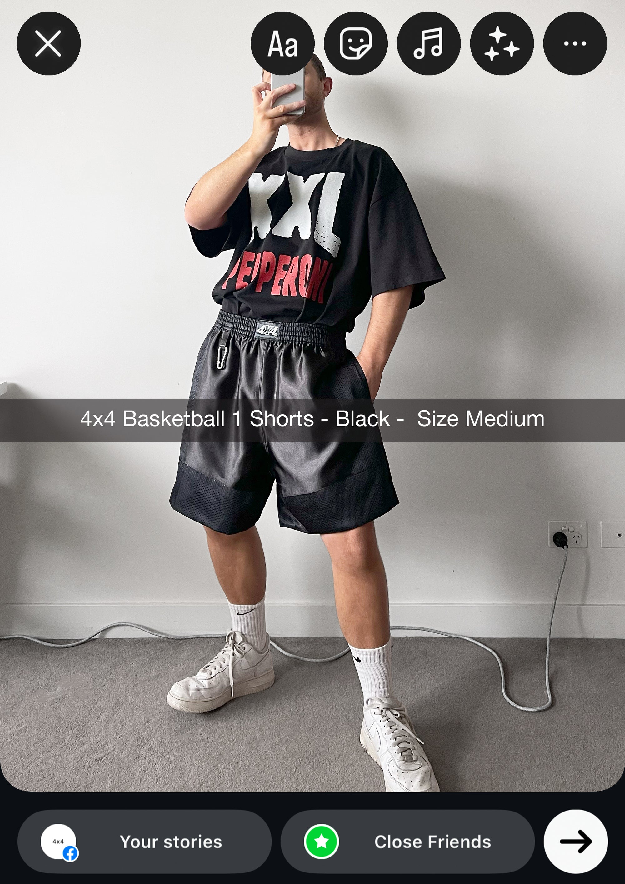 Person wearing a black t-shirt with red and white text and black shorts, standing against a plain wall.