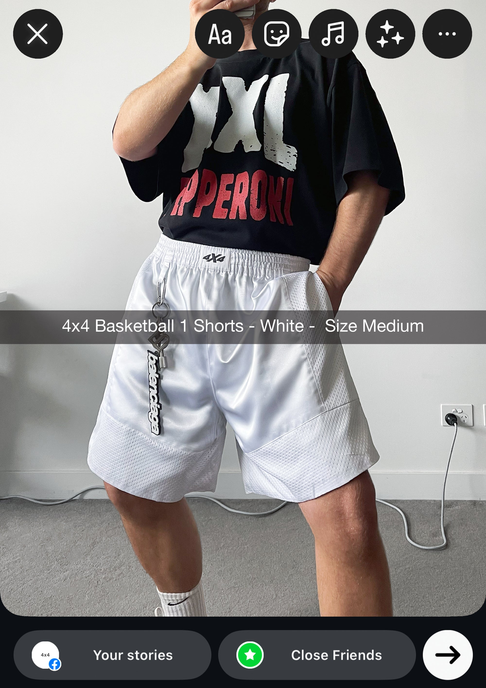 Person wearing a black oversized t-shirt with red and white text and white shorts in a room.