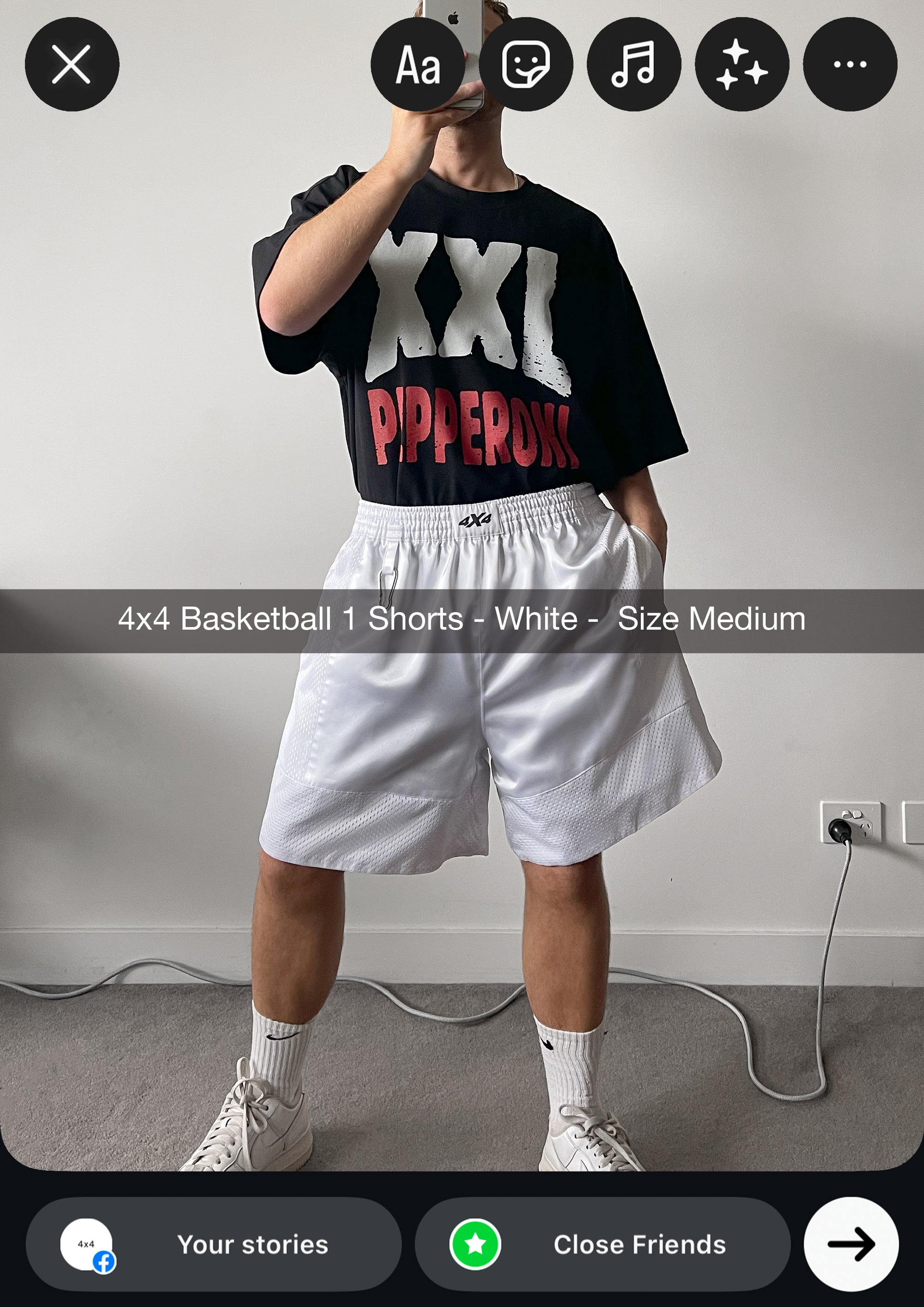 Person wearing a black t-shirt with white and red text and white shorts in a room.