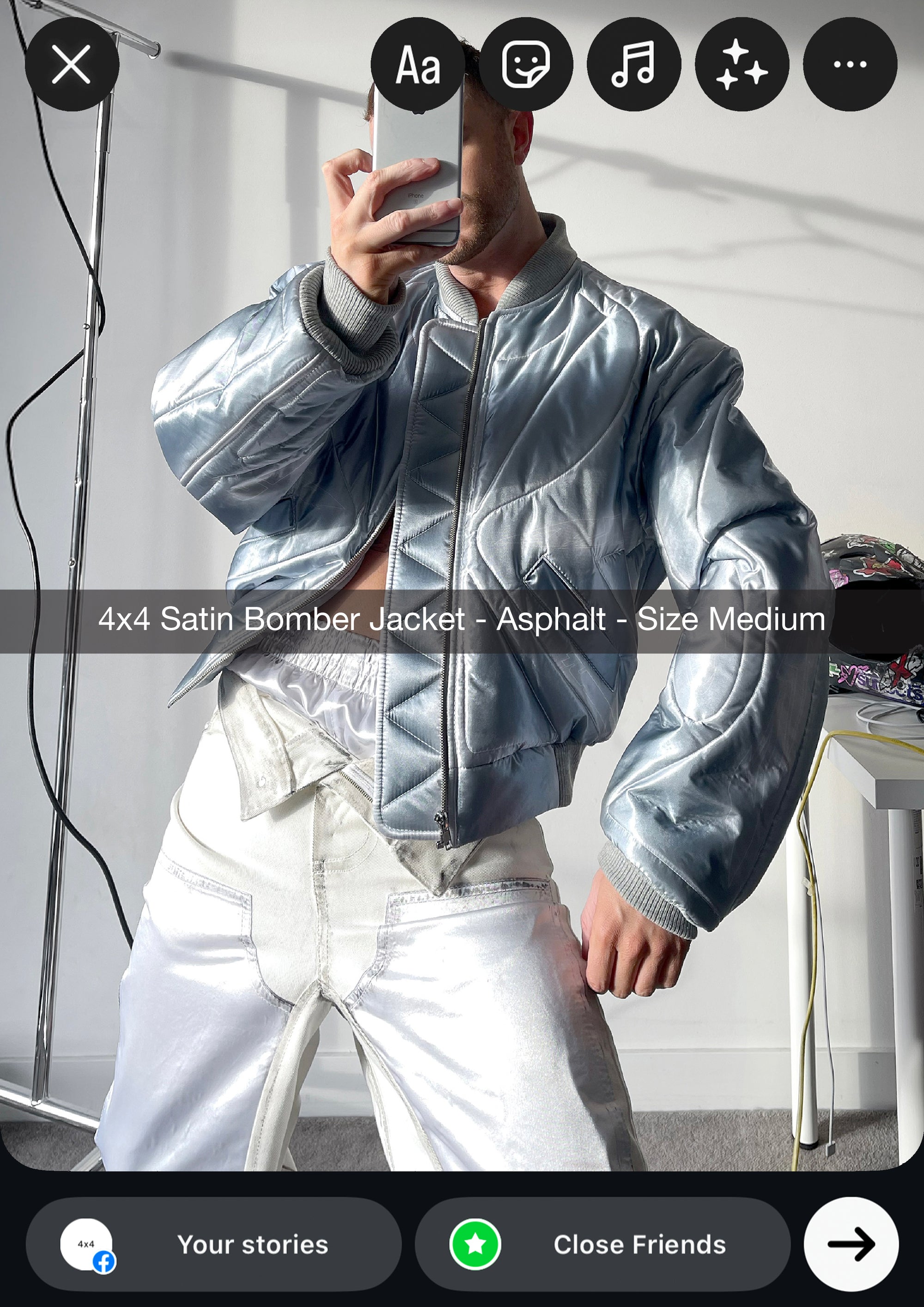Person wearing a silver satin bomber jacket taking a mirror selfie.